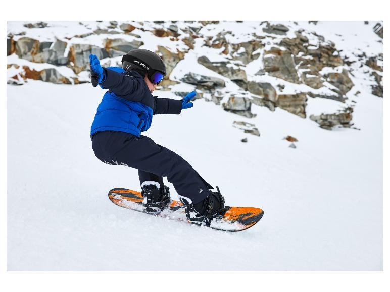 Un enfant snowboardeur porte un casque Crivit, des lunettes et une veste bleue.