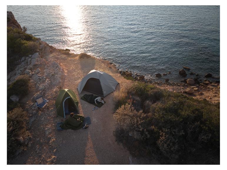 Deux tentes de camping et sacs de couchage sur une falaise au bord de la mer au coucher du soleil.