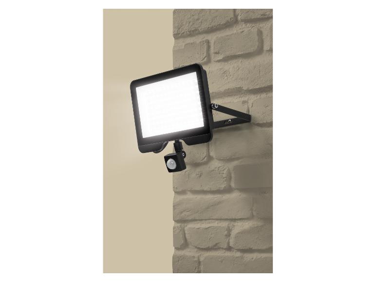 Lampe d'extérieur LED avec détecteur de mouvement sur un mur de briques beige.
