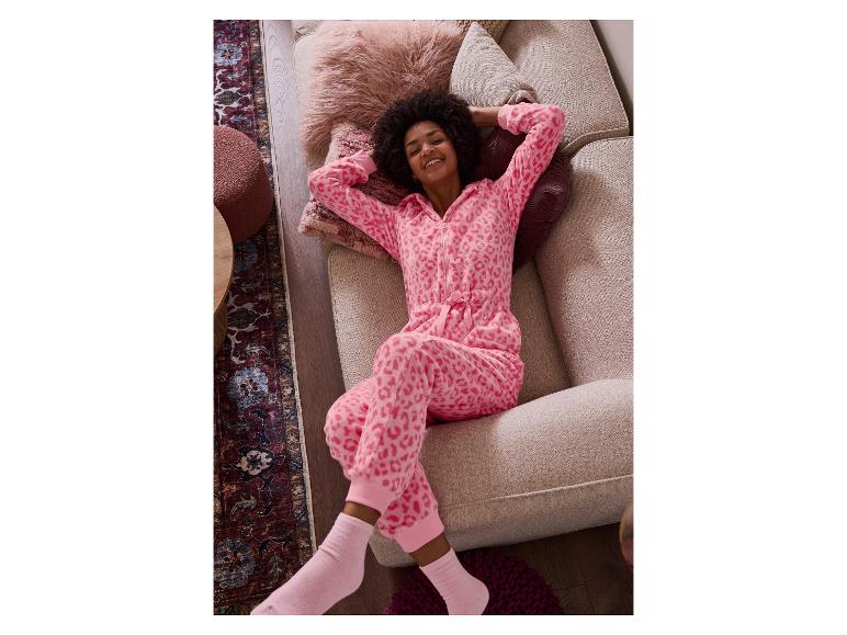 Femme en combinaison léopard rose, allongée sur un canapé beige.