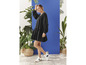Une femme en robe noire et baskets blancs pose parmi des plantes.