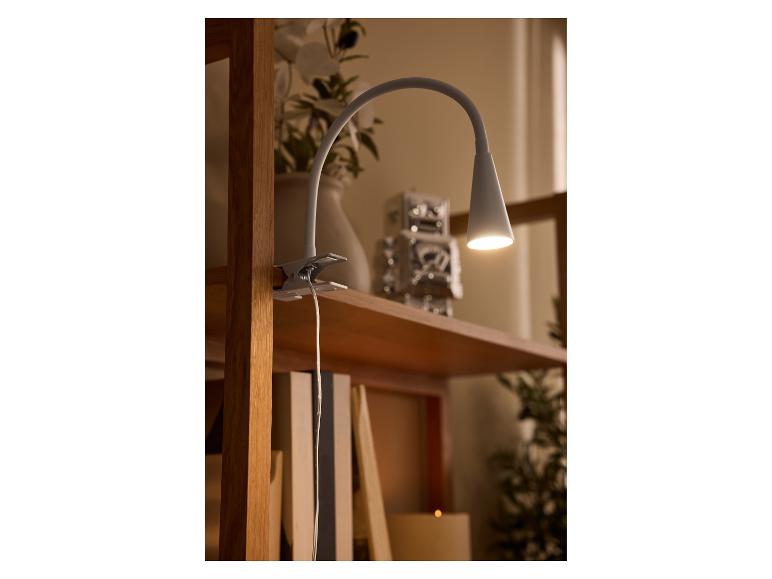 Lampe à pince blanche éclairant une étagère en bois avec décor.