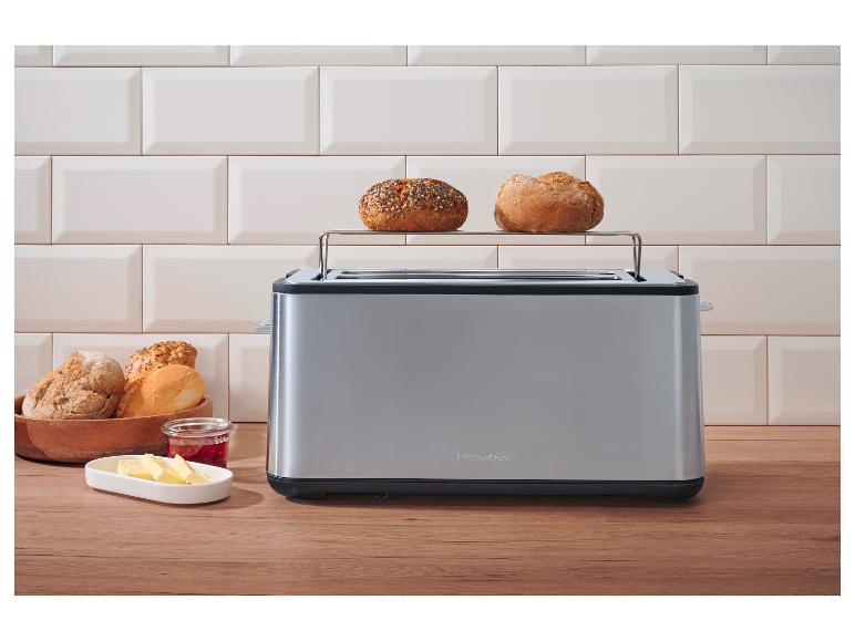 Grille-pain en acier inoxydable avec deux petits pains dessus, du beurre et de la confiture sur un comptoir en bois.
