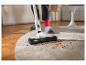 Personne nettoyant un tapis avec un aspirateur sans fil, ramassant des miettes.