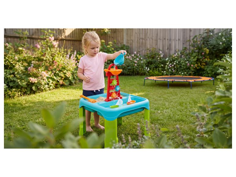 Fille joue avec une table eau-sable avec moulin et bateaux dans le jardin.