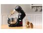 Un robot pâtissier noir avec de la pâte dans le bol et un pot de biscuits sur une table en bois.