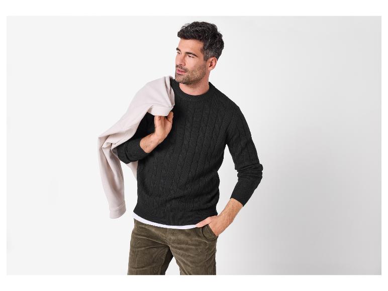 Homme en pull noir torsadé, pantalon en velours côtelé et veste beige sur l'épaule.