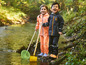Deux enfants en vêtements de pluie avec un filet et une pelle au bord d'un ruisseau.