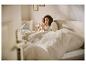 Femme souriante dans son lit, buvant dans une tasse, avec une literie confortable