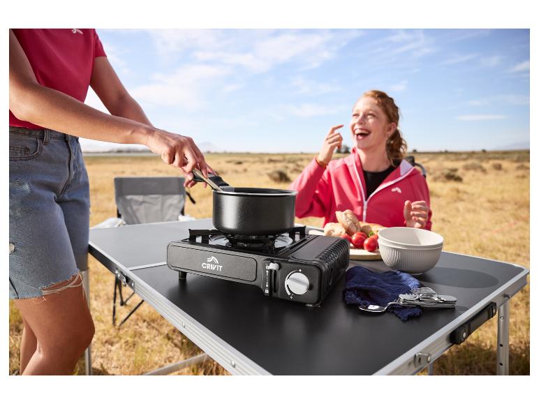 Une femme cuisine sur un réchaud à gaz portable, tandis qu'une autre rit en arrière-plan.