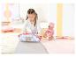 Fille jouant avec une poupée BABY born et un sac de couchage ours sur une couverture.