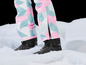 Des chaussures de ski noires Nitro avec un pantalon de ski rose et bleu.