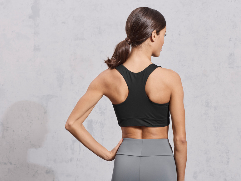 Une femme porte un soutien-gorge de sport noir et un legging gris.
