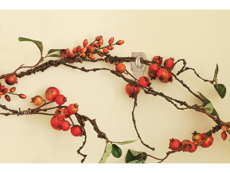 Guirlande décorative de baies rouges et de branches sur un mur clair.