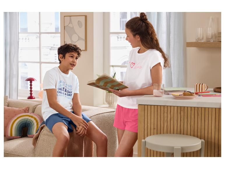 Deux enfants en t-shirts et shorts de pyjama, l'un avec un livre, dans le salon.
