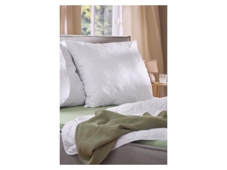 Oreillers et couette blancs sur un lit, avec plaid vert et draps.