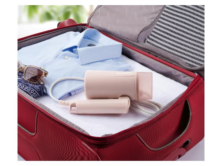 Un fer à repasser vapeur rose Silvercrest dans une valise rouge avec des vêtements.