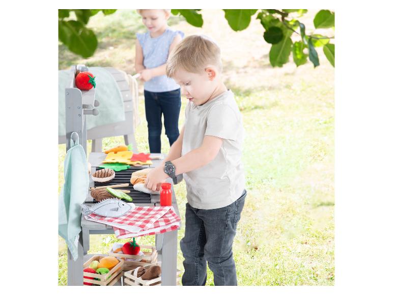 Enfants jouant avec un barbecue jouet et de la nourriture en feutre à l'extérieur.