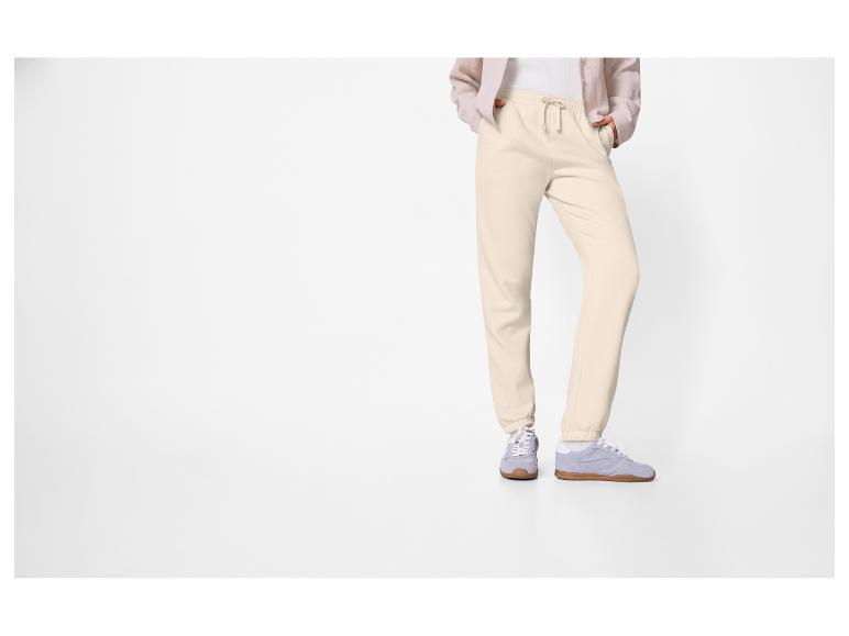 Personne portant un pantalon de survêtement crème et des baskets bleu clair.