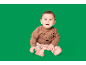 Bébé en pull marron avec un visage d'ours et un pantalon rayé, assis sur fond vert