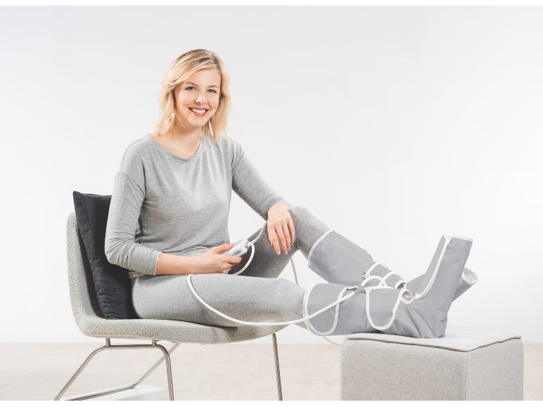 Une femme utilise un appareil de massage pour les jambes assise sur une chaise.