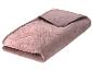 Une couverture matelassée pliée de couleur rose poudré avec un motif floral en relief.