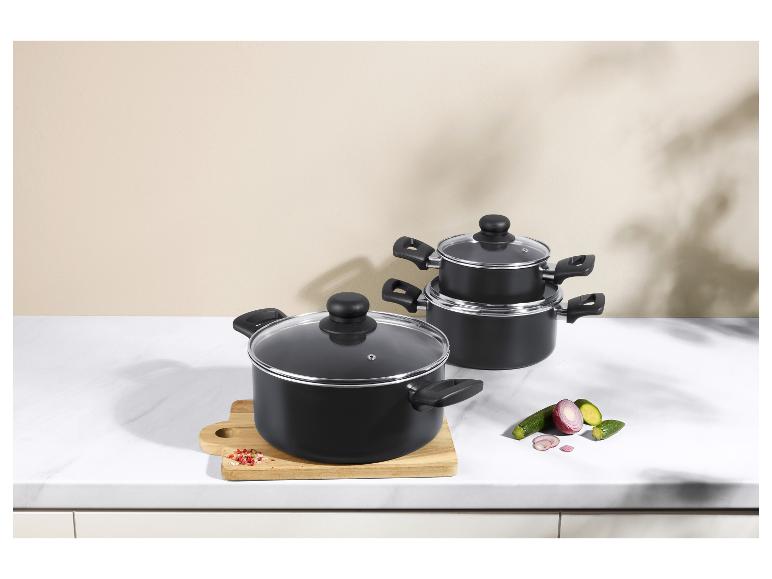 Casseroles noires avec couvercles en verre sur une surface en marbre blanc avec des légumes