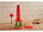 Mixeur plongeant rouge avec hachoir et verre doseur sur une surface en bois.