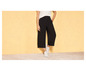 Une femme porte un pantalon noir large et des baskets blanches.