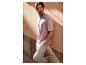 Homme en T-shirt rose et pantalon cargo kaki s'appuyant contre un mur.