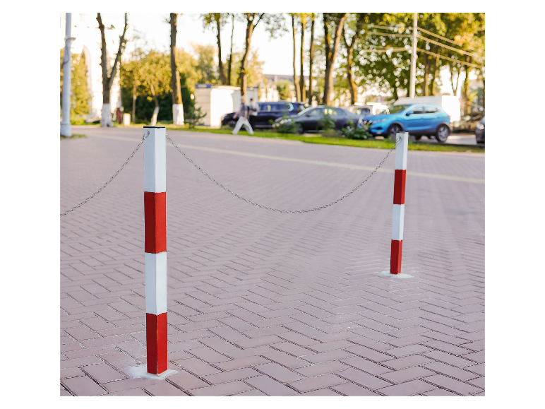 Deux poteaux blancs et rouges reliés par une chaîne dans un parking.