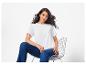 Femme en t-shirt blanc et jeans, assise sur une chaise en métal.