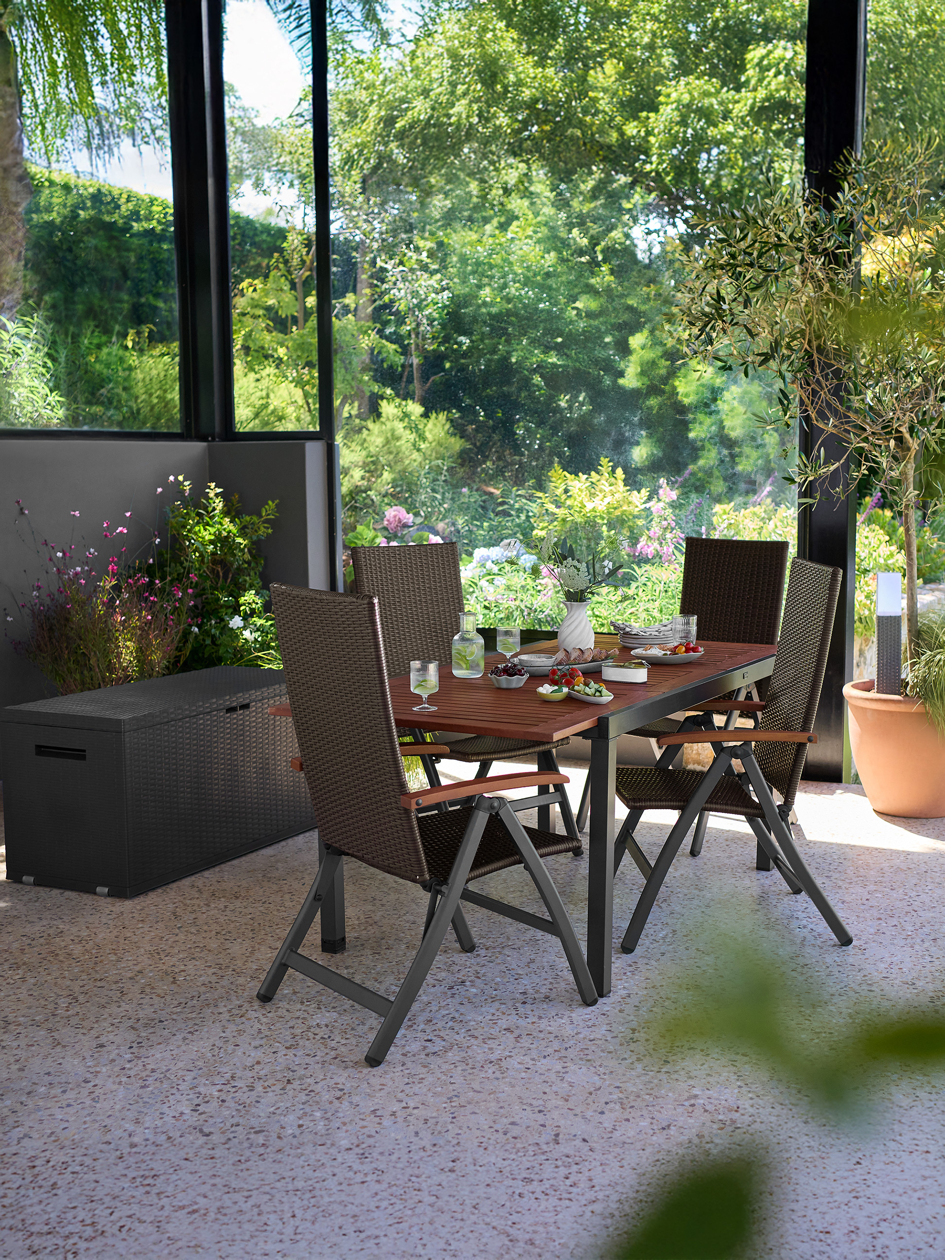Ensemble de salle à manger de patio avec chaises marron et table en bois, entouré de verdure.