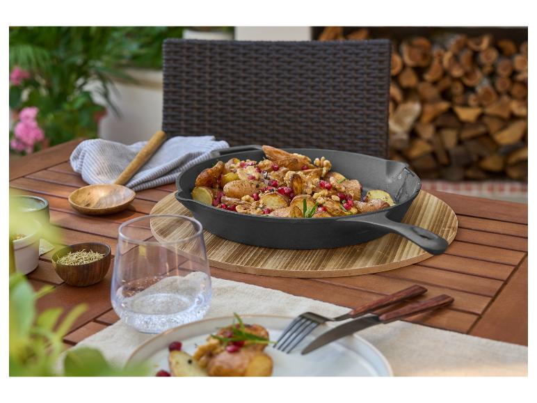 Poêle en fonte avec pommes de terre, grenade et noix sur une table en bois extérieure.