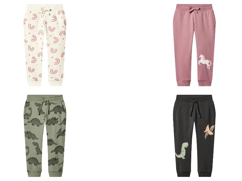 Quatre paires de pantalons de survêtement pour enfants : crème avec des arcs-en-ciel, rose avec une licorne, vert avec des dinosaures et gris foncé avec des dinosaures.