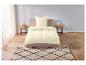 Un lit beige avec une couette, un oreiller et un tapis avec un motif géométrique noir.