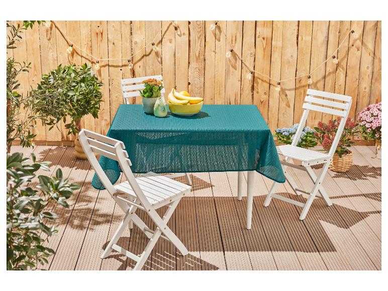 Table et chaises pliantes blanches, nappe turquoise, ambiance extérieure.