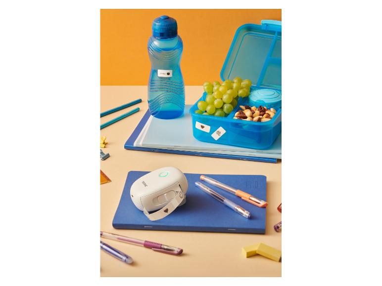 Boîte à lunch, bouteille d'eau et imprimante d'étiquettes avec fournitures scolaires sur la table.