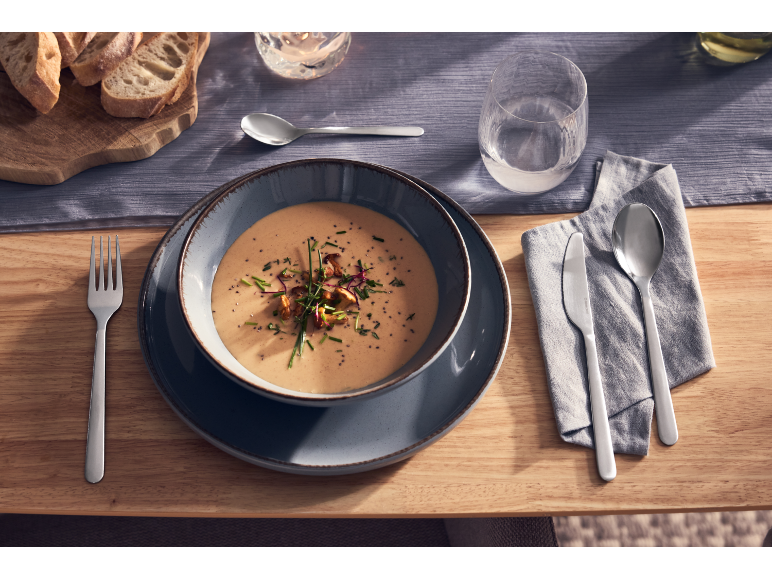 Un bol de soupe crémeuse servi avec des couverts et du pain sur une table dressée.