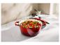 Cocotte en fonte rouge remplie de légumes sur un comptoir en marbre.