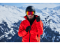 Homme avec casque de ski, lunettes et veste rouge dans les montagnes enneigées.