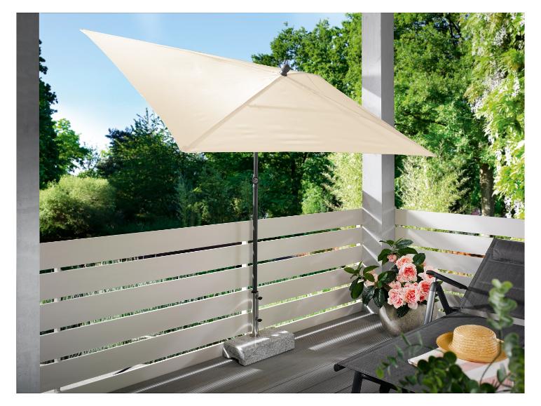 Un parasol beige sur un balcon avec un transat gris et un pot de fleurs roses.