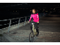 Femme en veste rose et pantalon noir sur vélo électrique la nuit