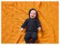 Bébé souriant en combinaison noire à capuche, allongé sur une couverture orange.