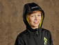 Un garçon porte une veste softshell noire avec une capuche verte.