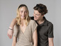 Une femme en robe beige et un homme en chemise vert foncé, riant ensemble.