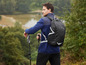 Un homme avec une veste polaire bleue, un sac à dos noir Crivit et des bâtons de randonnée dans la nature.