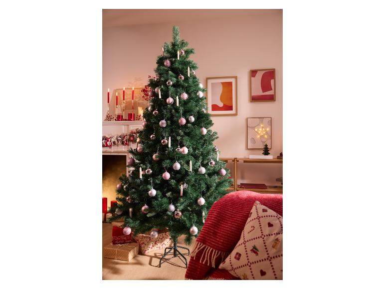 Sapin de Noël décoré d'ornements roses et argentés, près d'une cheminée avec des bougies.