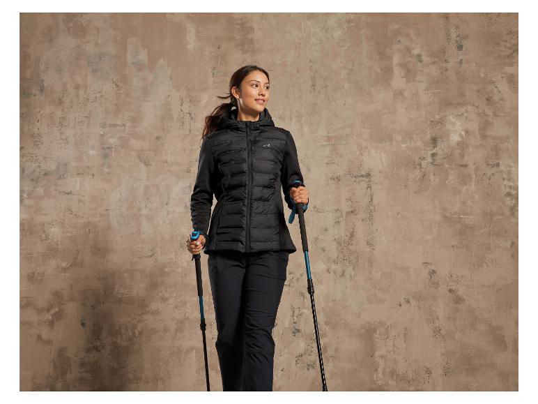 Une femme en veste d'hiver noire avec des bâtons de randonnée.
