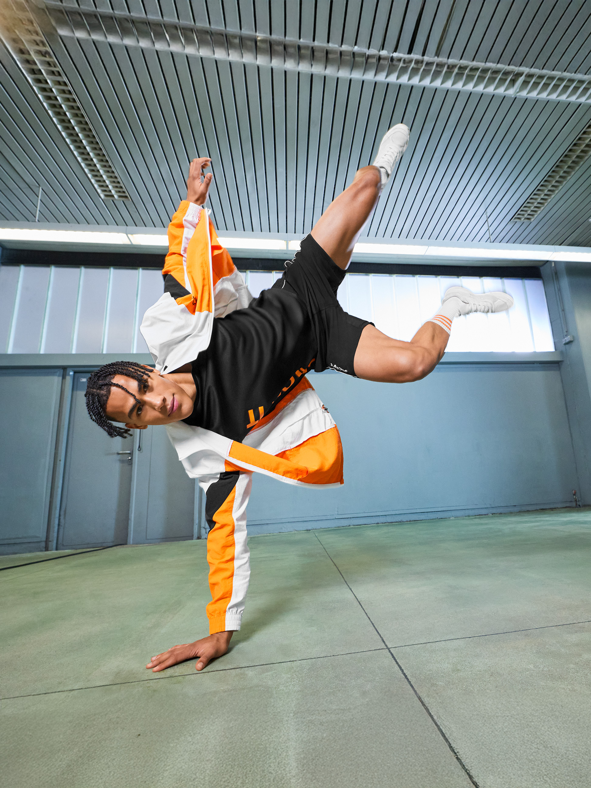 Homme en veste de sport orange et blanche et short noir exécutant un mouvement acrobatique.